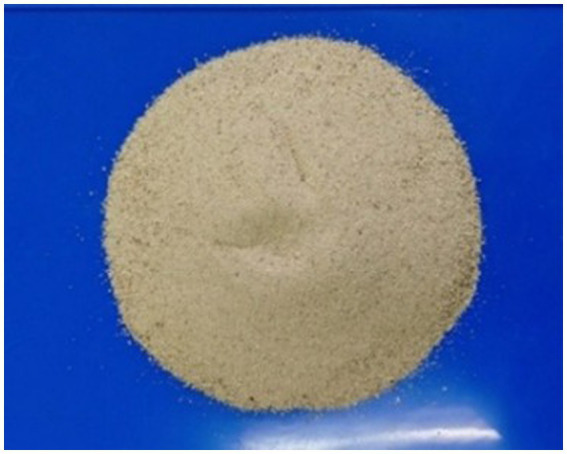 Fine beige powder is spread in a circular mound on a blue surface, with a small indentation in the center and some scattered grains around the edges.